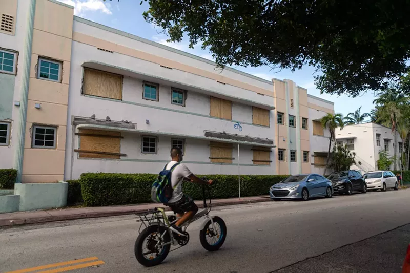Image: A man rides by a Miami Beach building with its windows boarded up on Thursday, August 30.