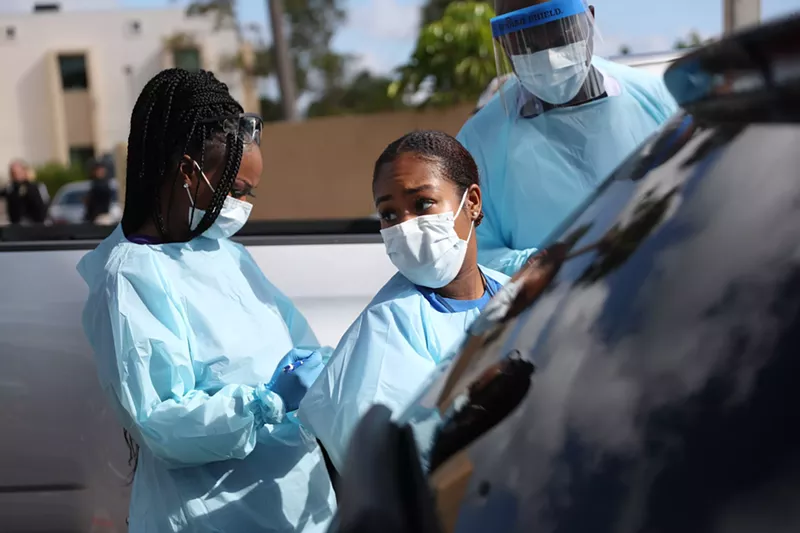 Image: Healthcare workers wear protective gear at a drive-thru testing center in West Palm Beach.