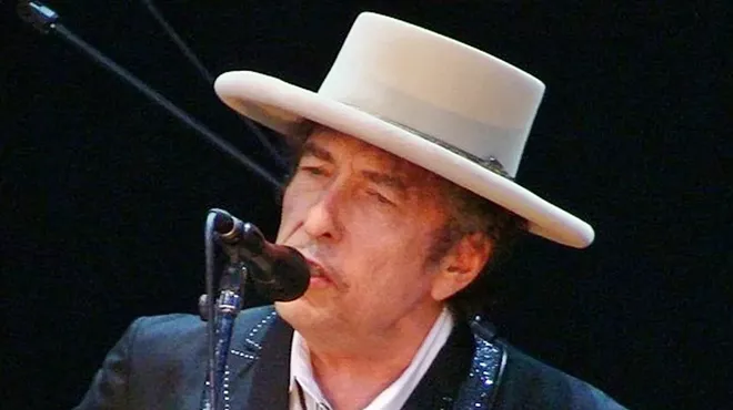 headshot of an older bob dylan performing, sporting a wide-brimmed hat