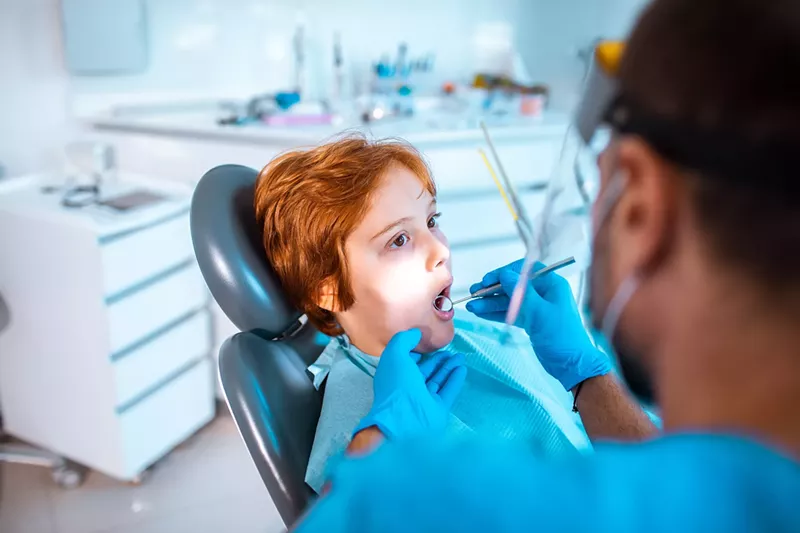 Image: Young boy in a dentists office having work done on his teeth by a male dentist